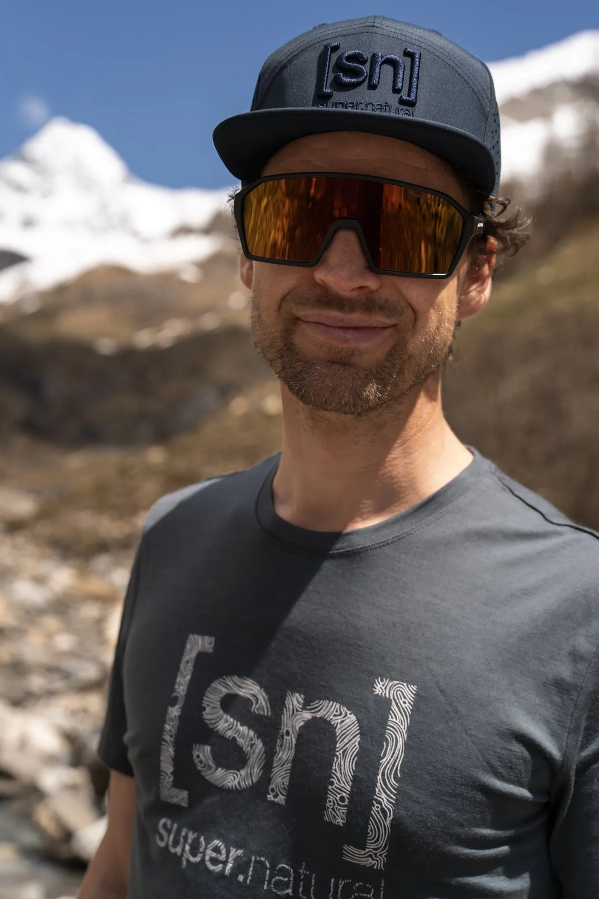 Porträt von Thilo mit [sn]-Cap und super.natural-Shirt vor Schneebergen