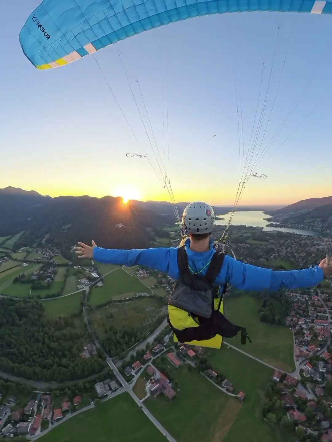 Thilo im Gleitschirm mit ausgebreiteten Armen, Sonnenuntergang über dem Tegernsee